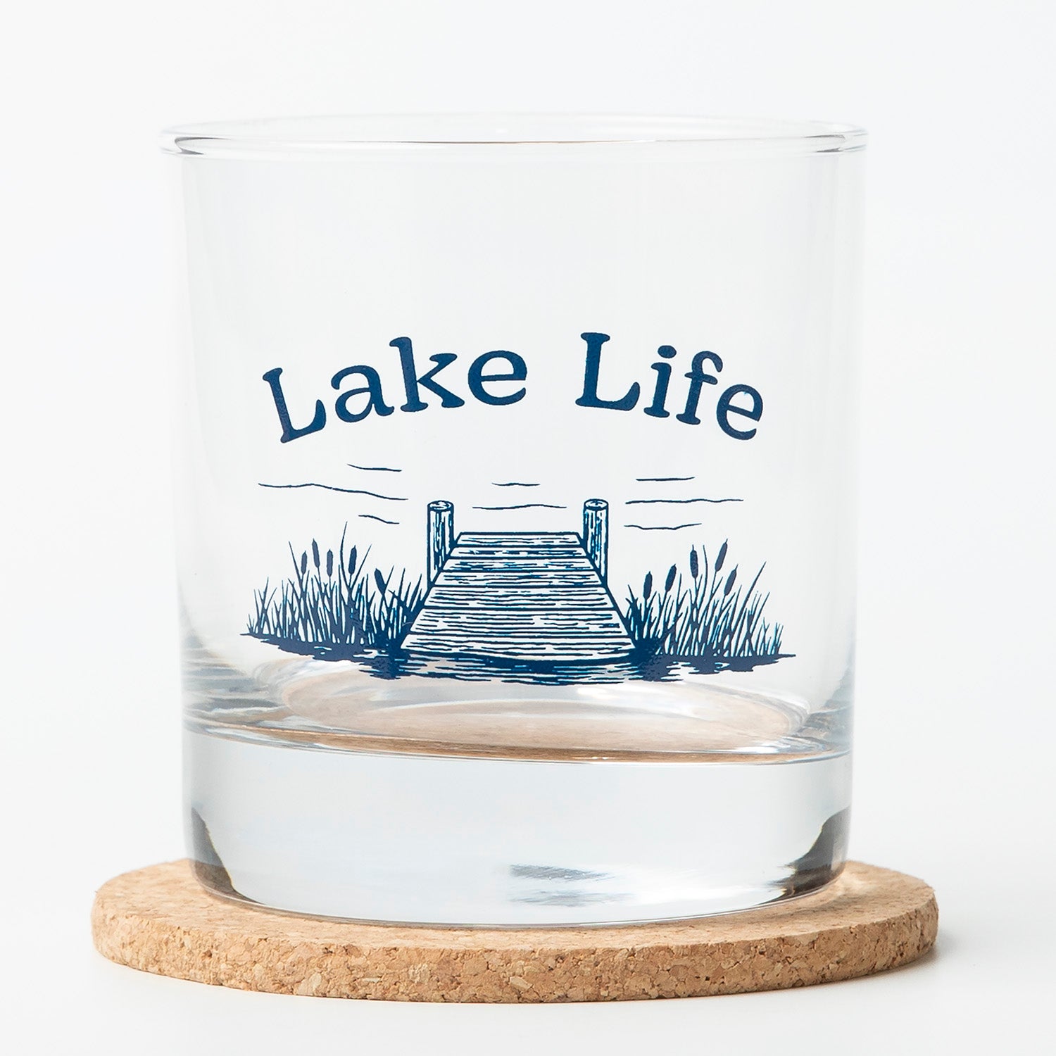 Whiskey glass with 'Lake Life' text and lake dock graphic, sitting on a cork coaster.