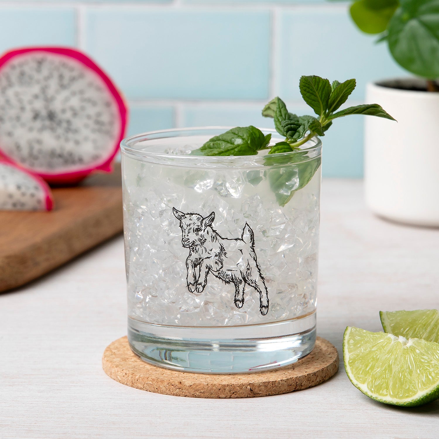 Goat etched whiskey glass with ice and mint, lime wedge, dragon fruit in kitchen setting