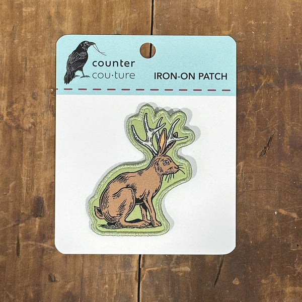 An iron-on patch depicting a rabbit with antlers, which is part of a larger package labeled "counter cou-ture iron-on patch".