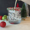Pouring a festive drink into a whiskey glass which is printed with antlers and has red and green sprinkles on the rim.