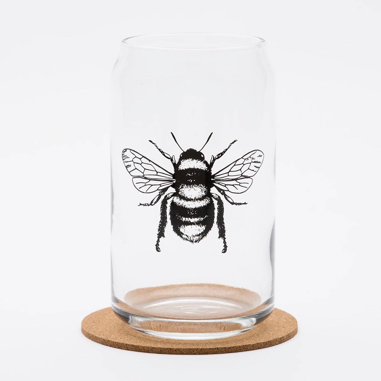 Clear beer can glass with detailed black bee illustration on front, sitting on cork coaster