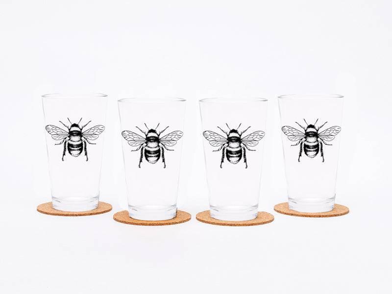 Set of four pint glasses with black bee illustration, each on a cork coaster, white background