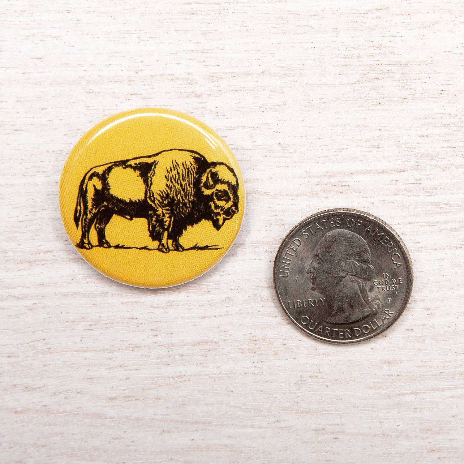 Yellow bison illustration button pin next to a US quarter on light wood surface