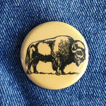 Round yellow button pin with black bison illustration on blue denim fabric background