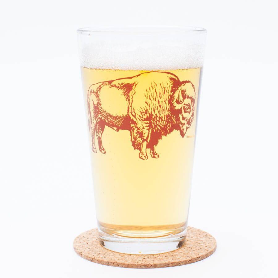 Pint glass with buffalo design filled with beer, resting on a cork coaster on white background