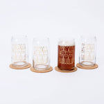 Set of four cat can glasses with gold cat illustrations, one filled with beer on cork coasters