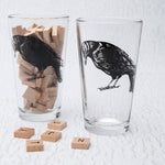 Set of pint glasses with black raven illustration, wooden letter tiles inside and around glasses