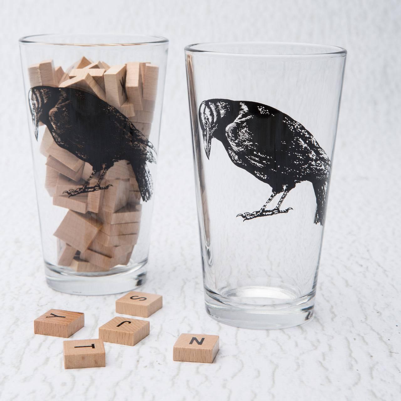 Set of pint glasses with black raven illustration, wooden letter tiles inside and around glasses