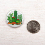 Round cactus button pin with potted cactus illustration next to a US quarter on wood surface