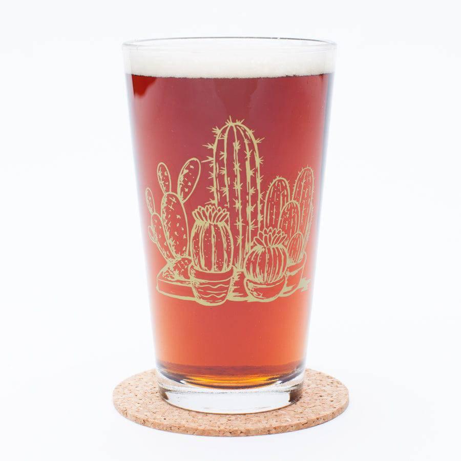 Pint glass filled with amber beer, etched with assorted cactus designs on a cork coaster