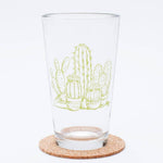 Clear pint glass with green cactus illustration, placed on a cork coaster
