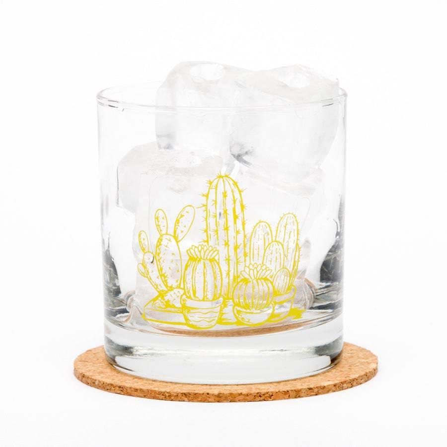 Whiskey glass with yellow cactus illustration, filled with ice, on a cork coaster