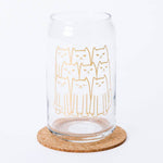 Clear can-shaped glass with cute gold line art cat design, placed on a cork coaster