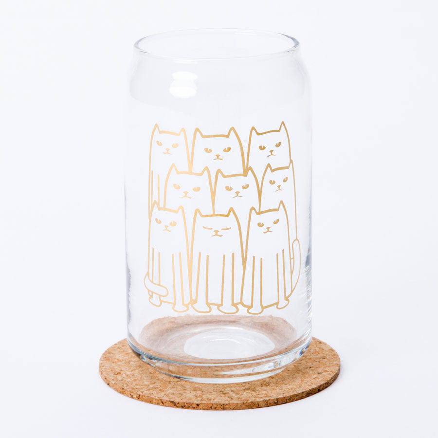 Clear can-shaped glass with cute gold line art cat design, placed on a cork coaster