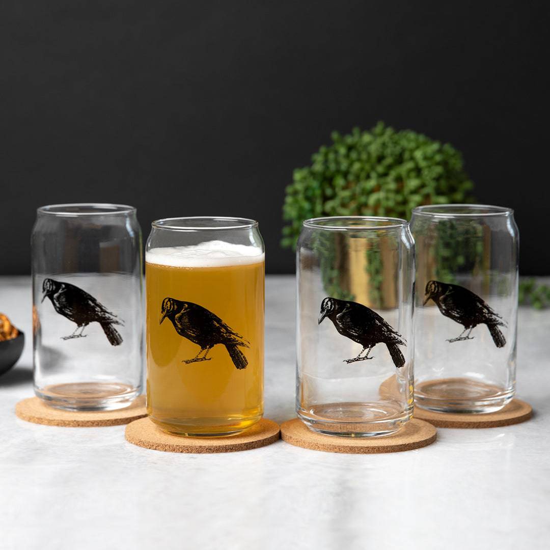 Set of four can-shaped beer glasses with black crow illustrations, one filled with beer.