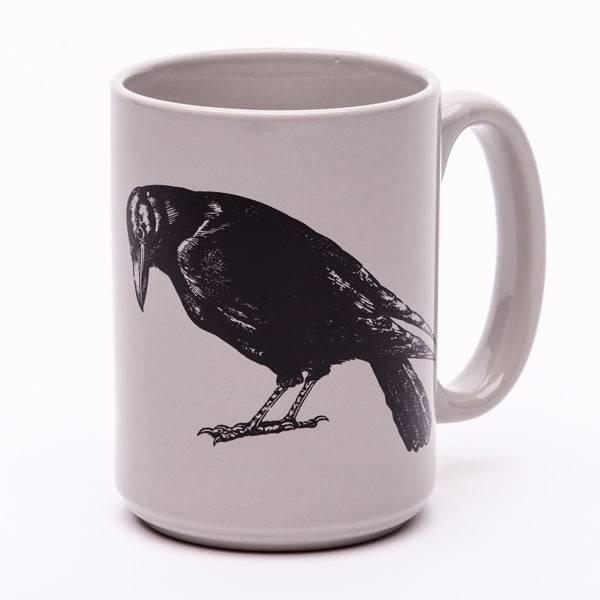 White ceramic mug featuring a detailed black crow illustration, isolated on white background