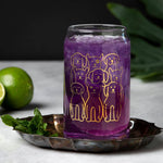 Dog can-shaped glass with gold dog illustrations, filled with purple drink on a tray
