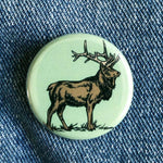Round elk illustration button pin on denim fabric, rustic nature-themed accessory