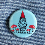 Round pin button with a gnome and red mushrooms on denim fabric background