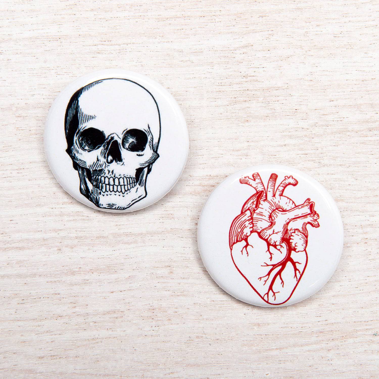 Round pinback buttons featuring a skull and anatomical heart illustration on white background