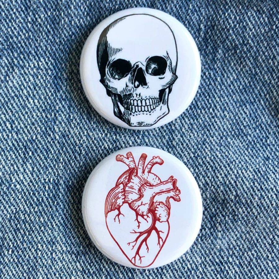 Heart and skull graphic pins on denim background, anatomical design novelty buttons