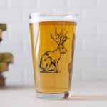 Pint glass with jackalope illustration, filled with beer, set on a light surface