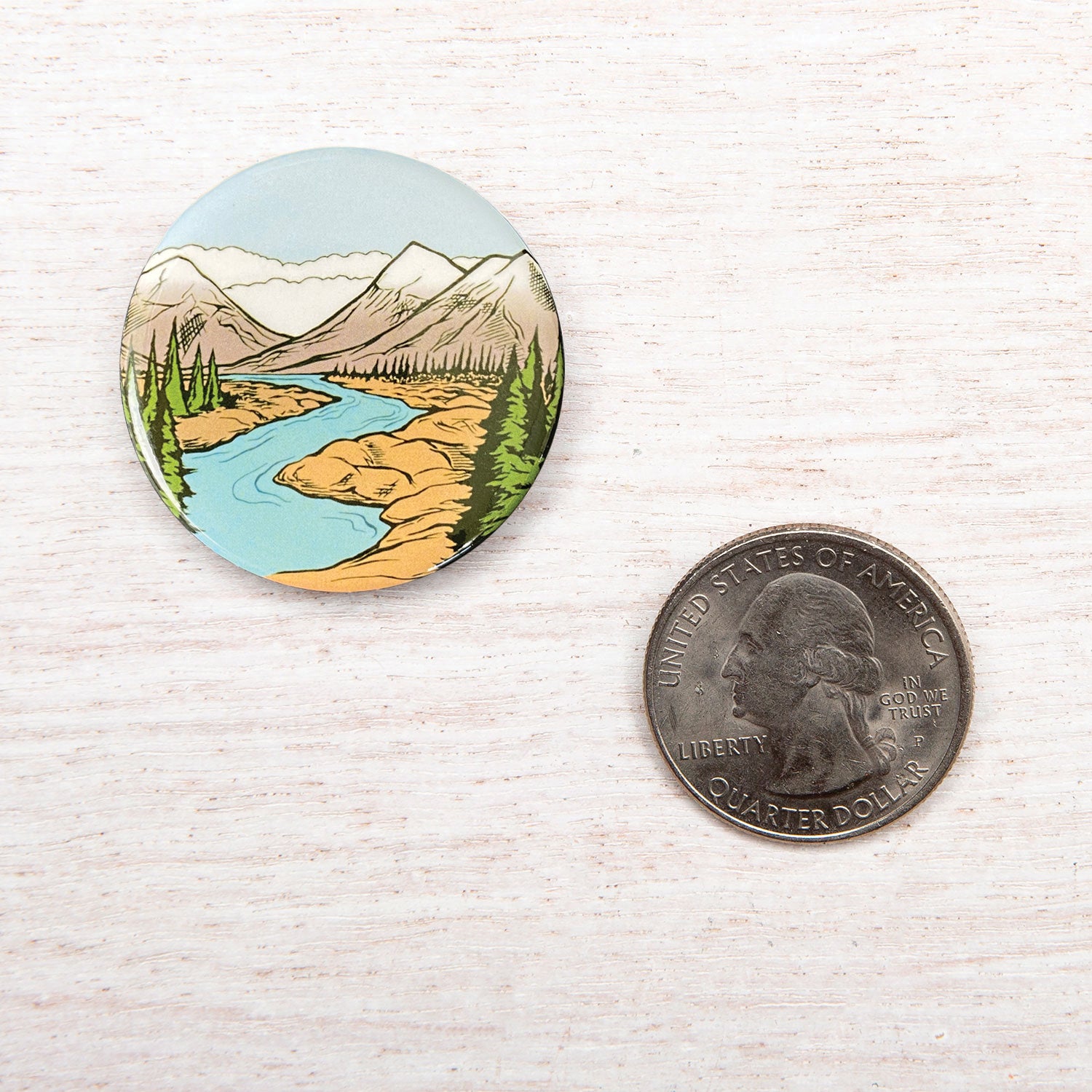 Round mountain river landscape button pin next to a US quarter for size comparison