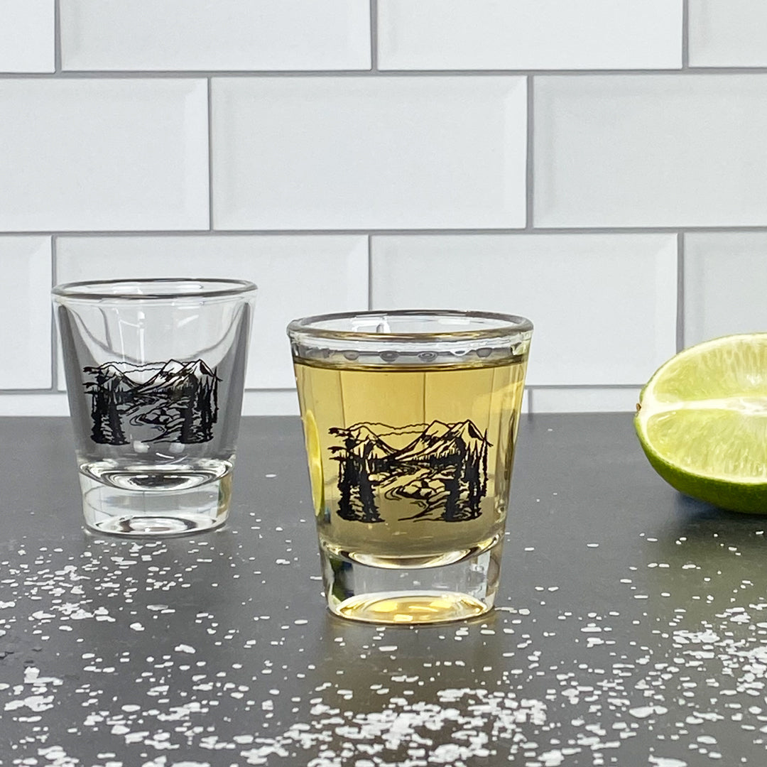 Two mountain design shot glasses on a counter with lime and salt, subway tile background