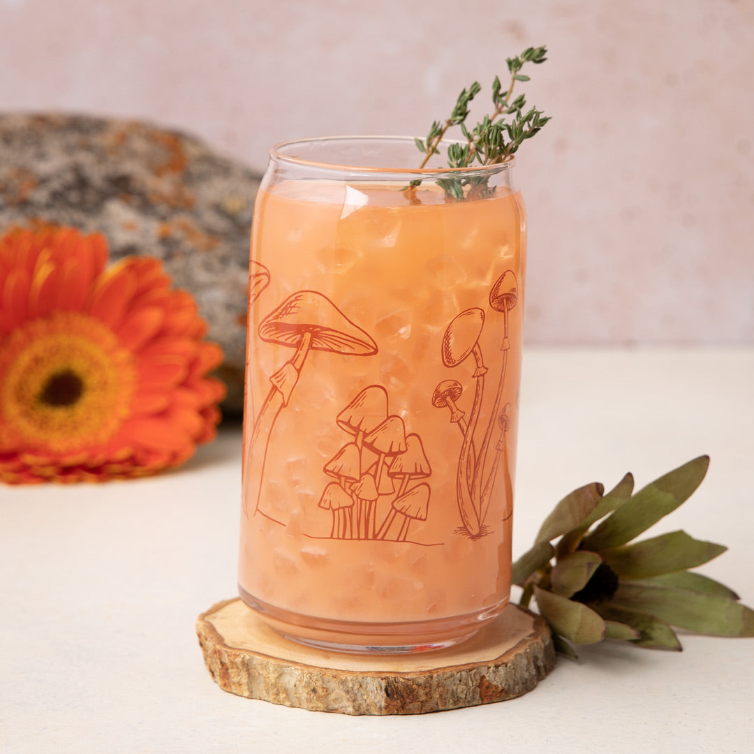 Iced orange drink in mushroom can glass with wood coaster, flower, and succulent accents