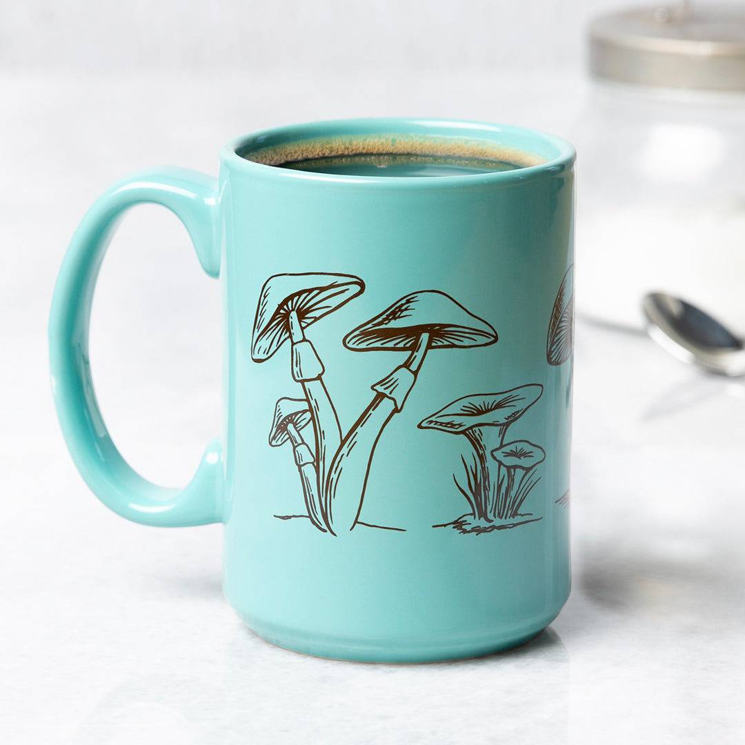Aqua ceramic coffee mug with black mushroom illustration, on a kitchen counter.