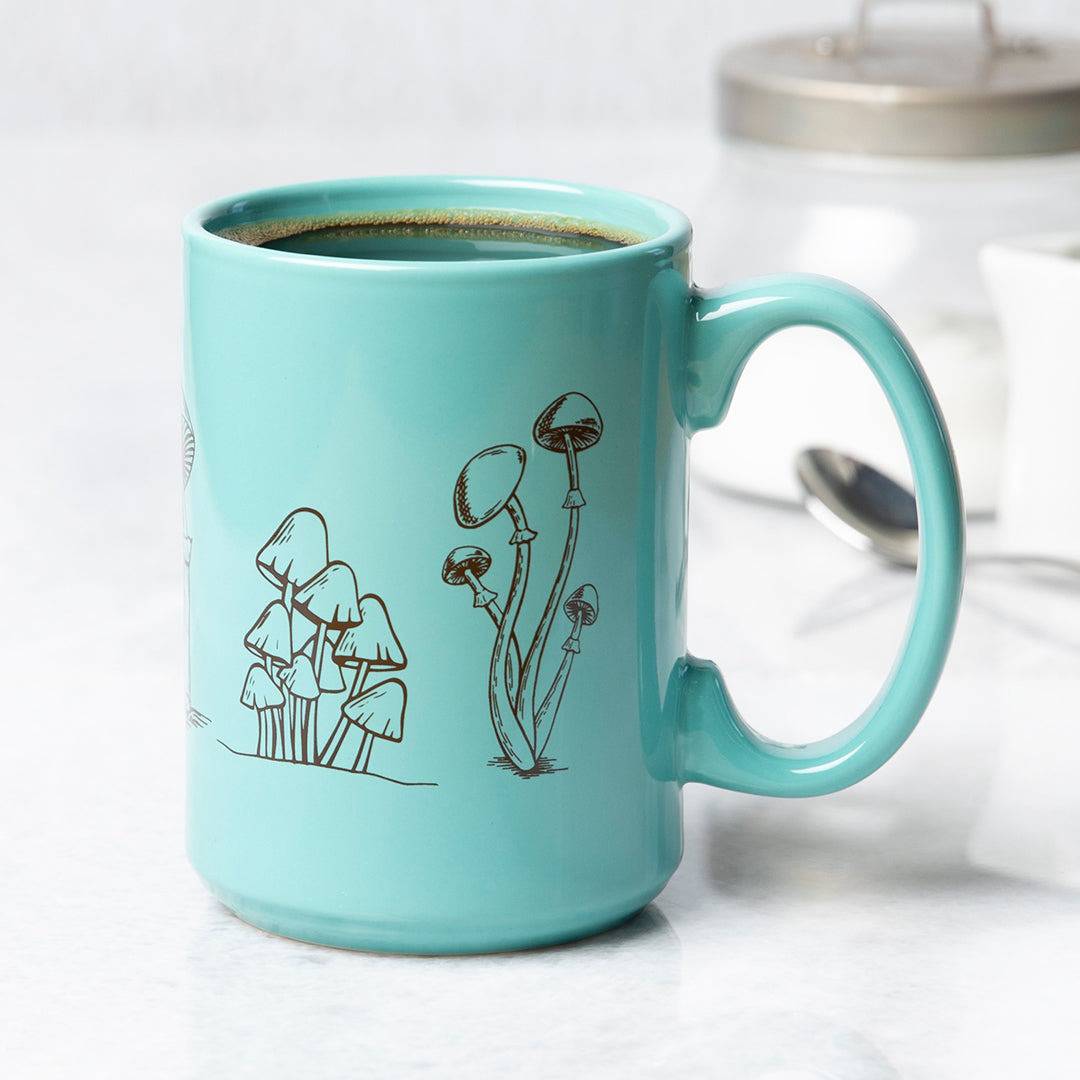 Turquoise ceramic mug with black mushroom illustrations, filled with coffee on kitchen counter
