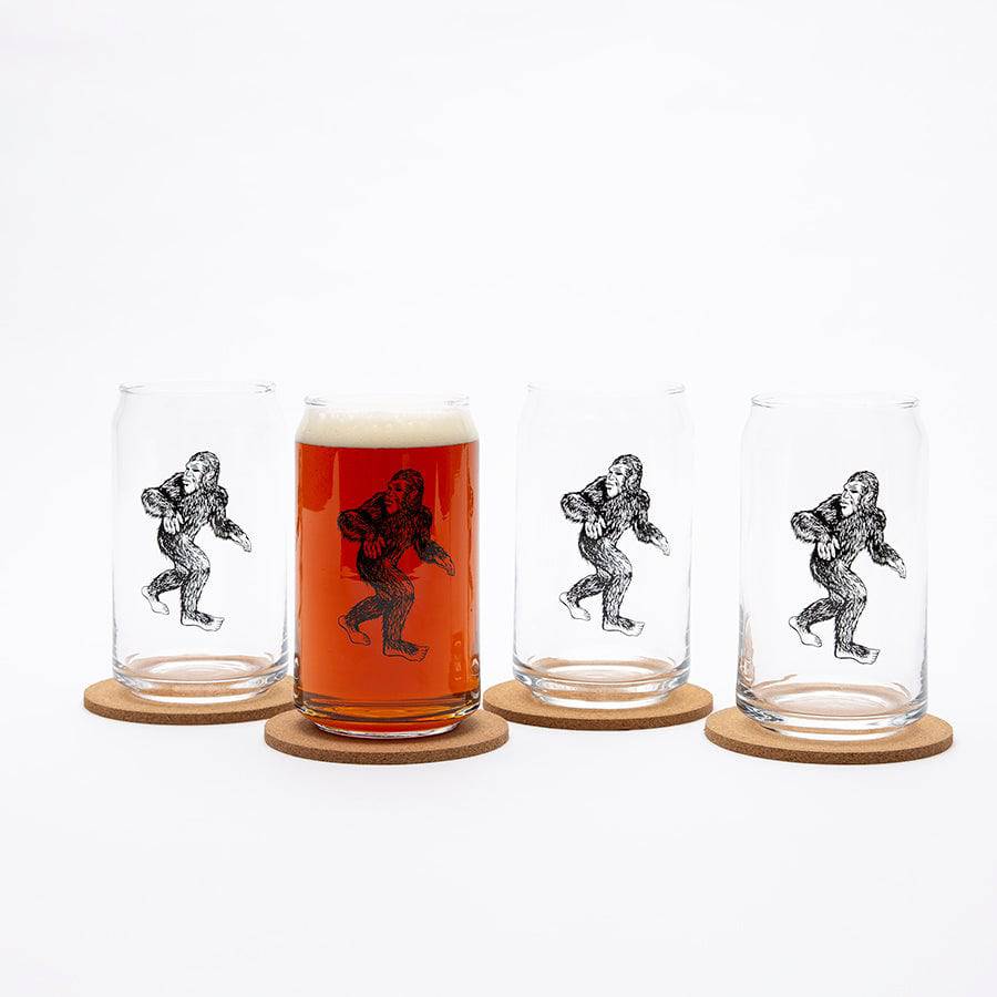 Set of four clear can-shaped beer glasses with black Sasquatch design on cork coasters