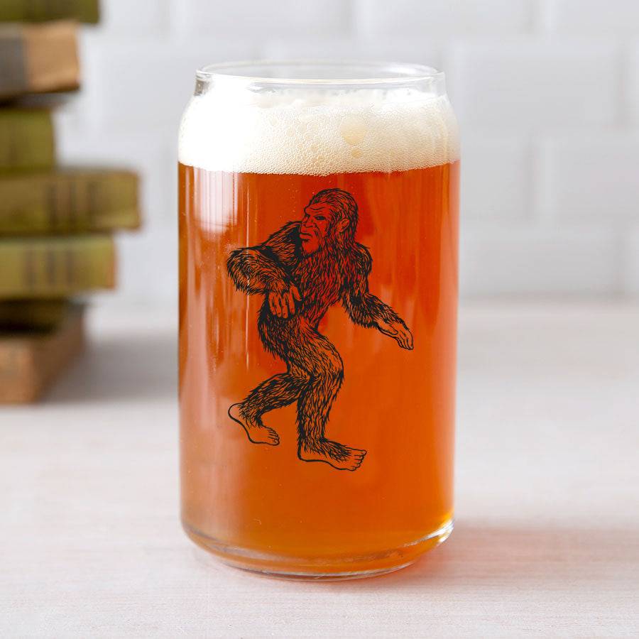 Can-shaped beer glass with black Sasquatch graphic, filled with amber beer and foam