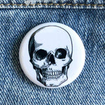 White button pin with black skull illustration on blue denim fabric