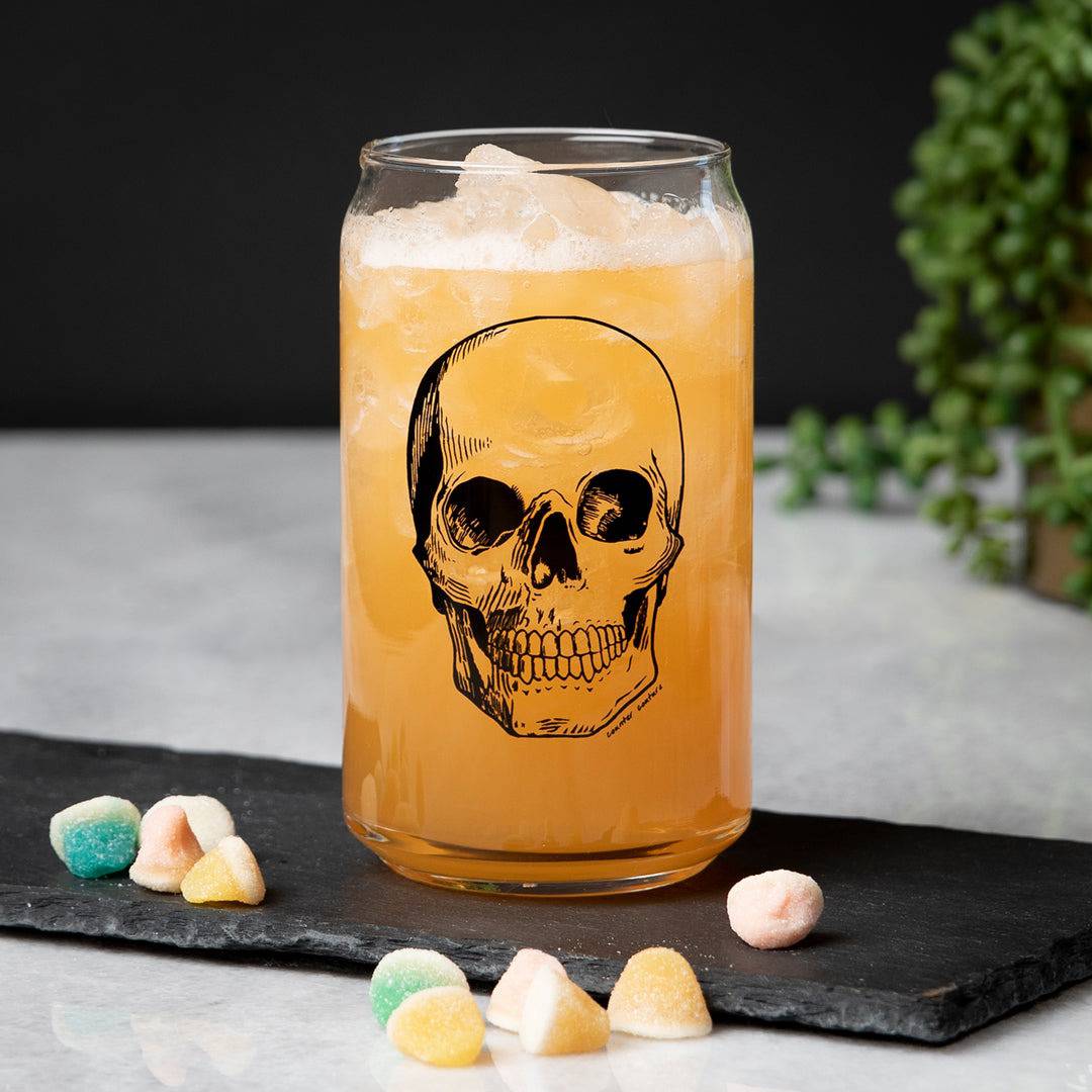 Skull can glass with orange drink and ice, surrounded by colorful gummy candies