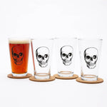 Set of four pint glasses with black skull design, one filled with beer on coasters
