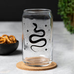 Clear can-shaped glass with black snake and star design, modern barware on a cork coaster.