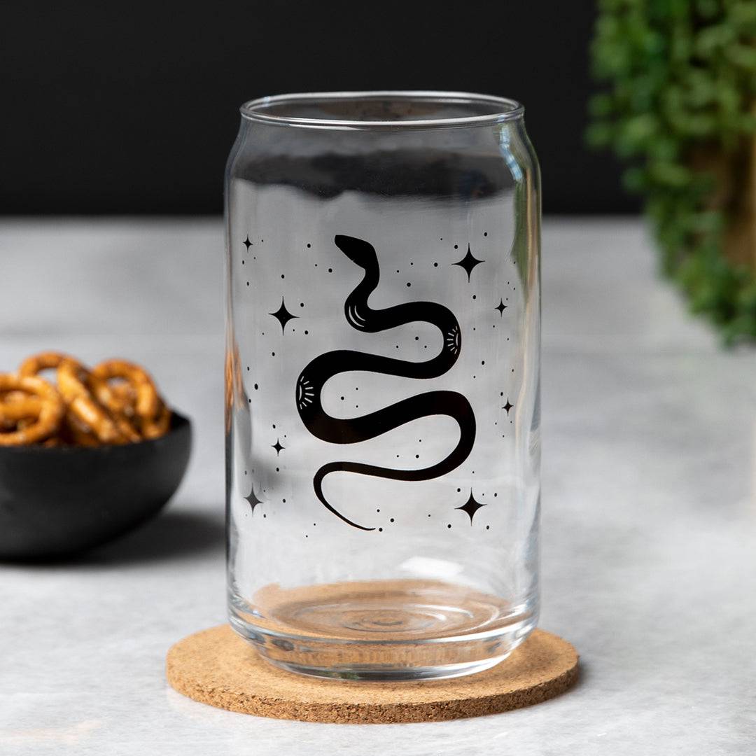 Clear can-shaped glass with black snake and star design, modern barware on a cork coaster.