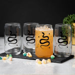 Set of four clear can-shaped glasses with black snake design on a marble surface, one filled with iced drink.