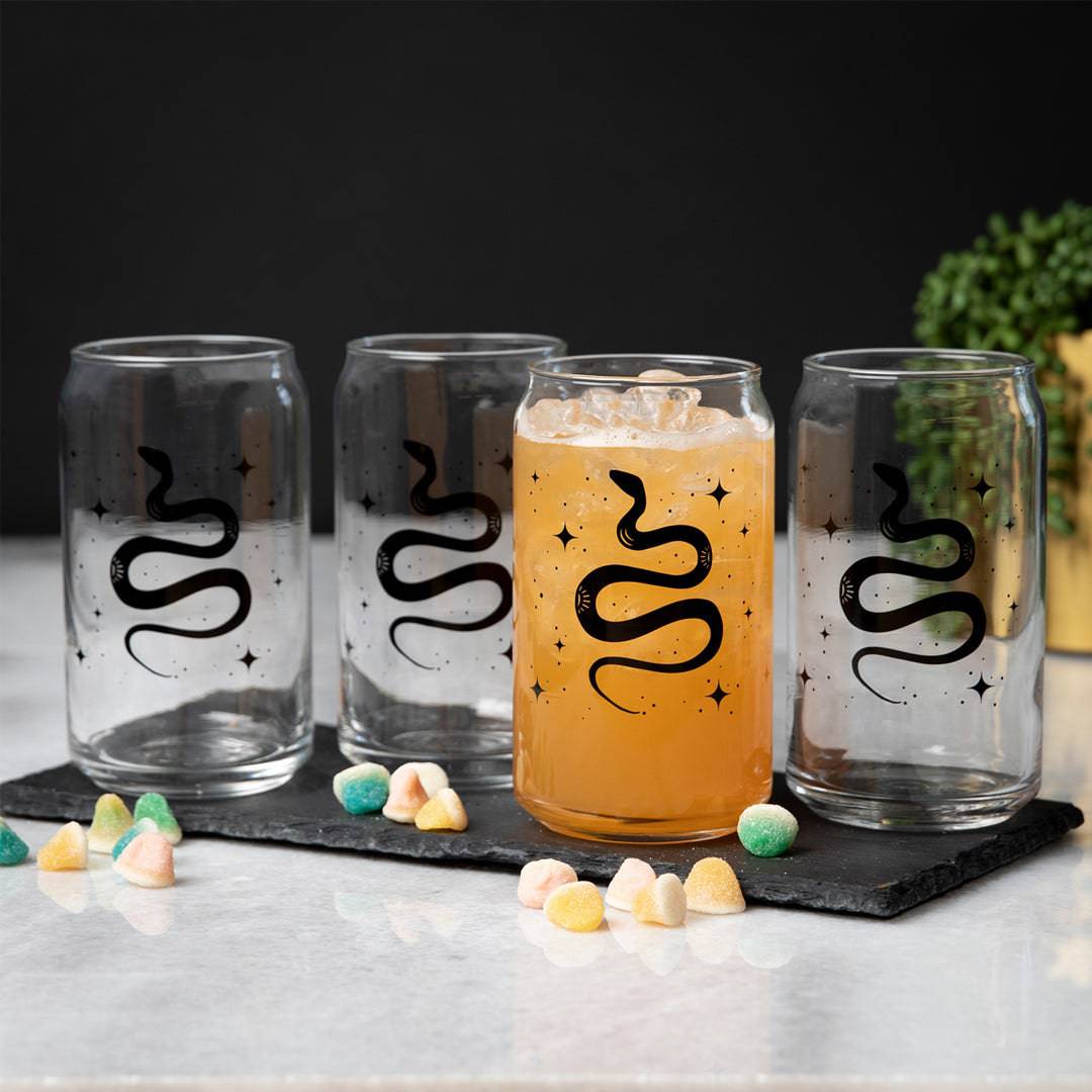 Set of four clear can-shaped glasses with black snake design on a marble surface, one filled with iced drink.