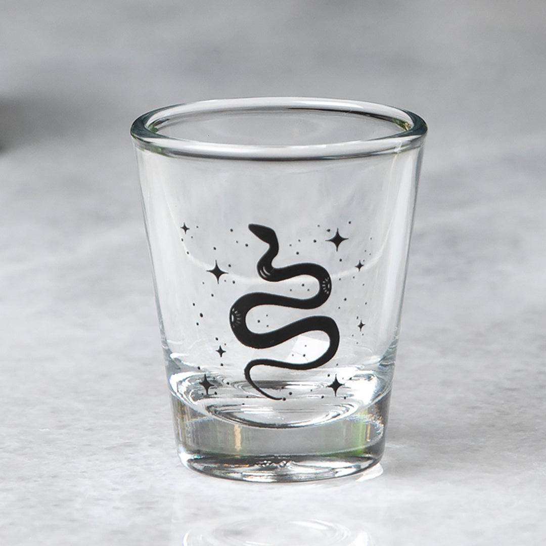 Clear shot glass with black snake and star design on marble surface