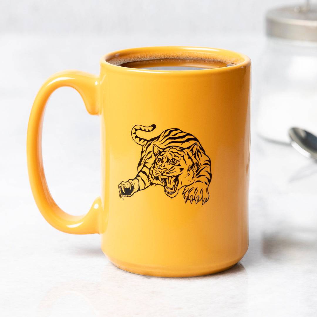 Yellow ceramic mug with black tiger illustration, filled with coffee on a white countertop