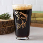 Pint glass of dark beer with etched trout fish design, on a rustic wooden table.