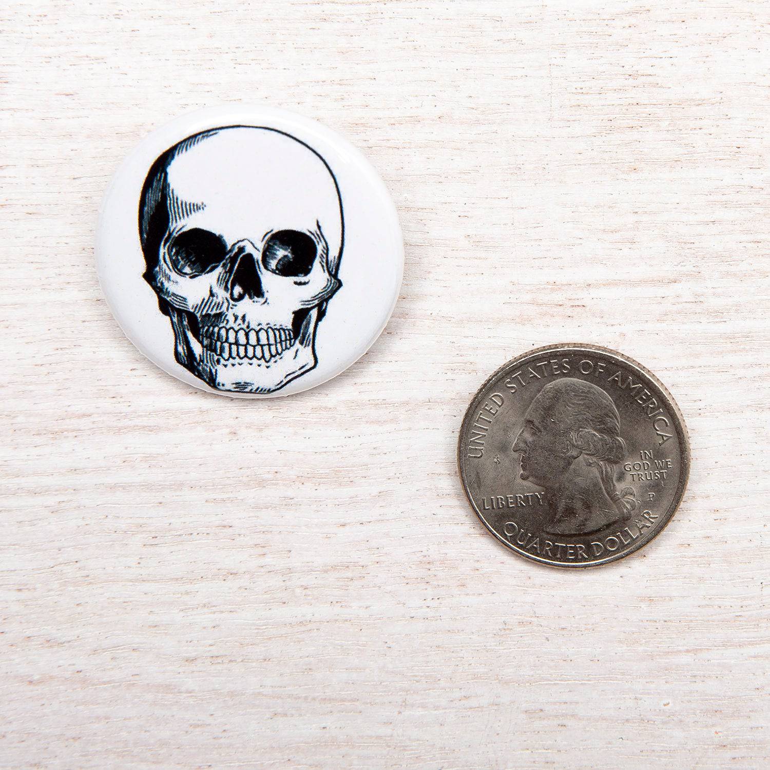 Round magnet with black skull illustration next to a US quarter on light wood surface